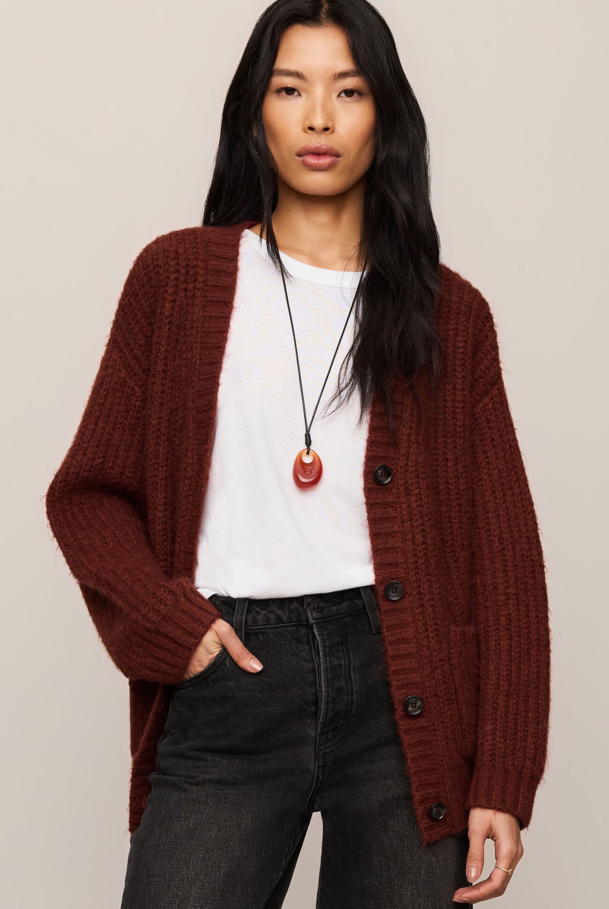 Woman wearing a burgundy cardigan over a white shirt with black pants on a beige background