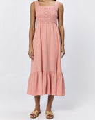 A woman standing, wearing a terracotta sleeveless maxi dress with a square neckline and lace detailing on the chest.