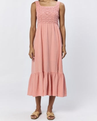 A woman standing, wearing a terracotta sleeveless maxi dress with a square neckline and lace detailing on the chest.