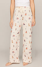 A person wearing cream-colored wide-leg pajama pants with a colorful cartoon rabbit and star print, paired with a white tank top, shown against a neutral studio background.
