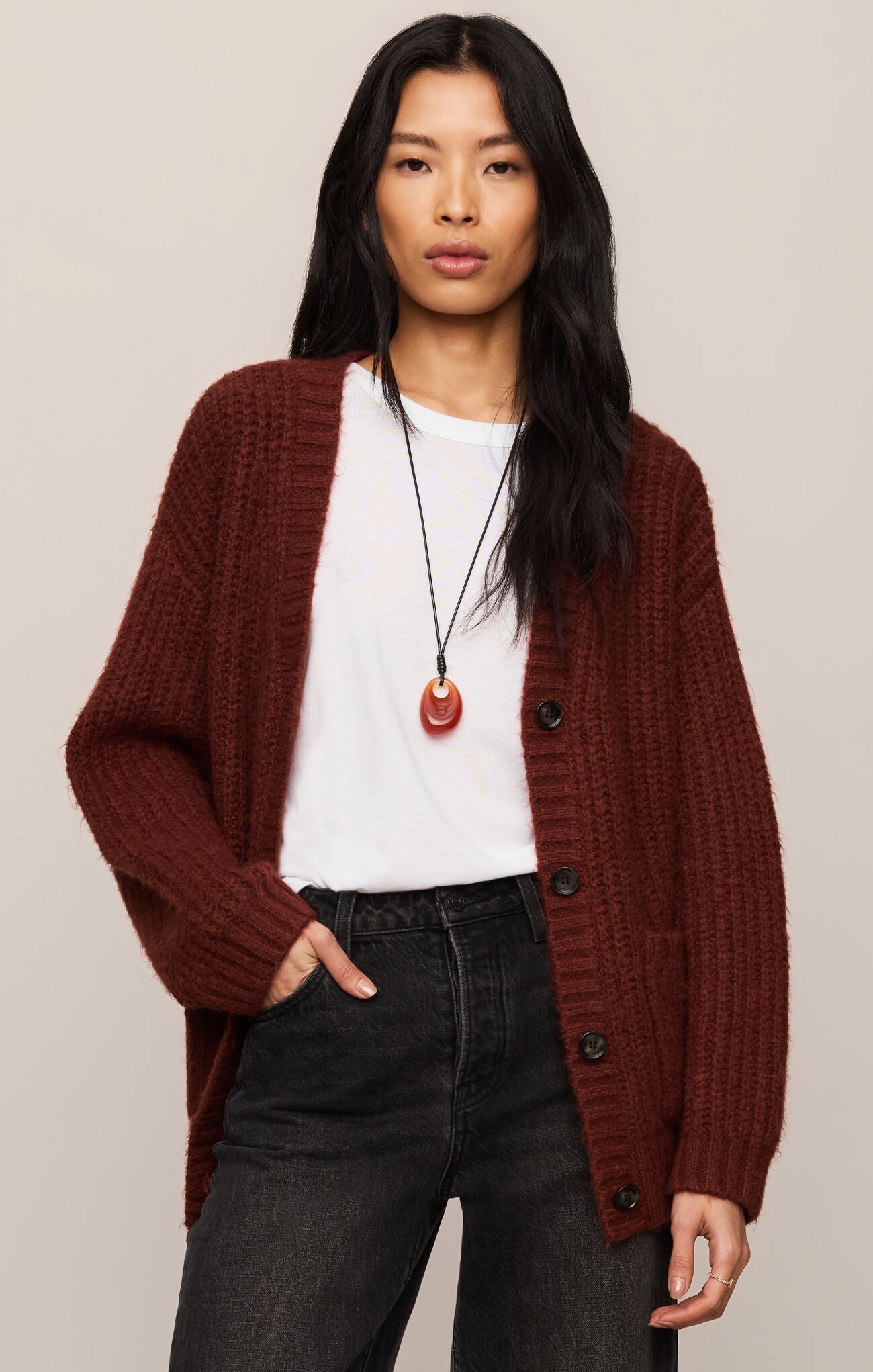 Woman wearing a burgundy cardigan over a white shirt with black pants on a beige background