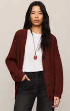Woman wearing a burgundy cardigan over a white shirt with black pants on a beige background